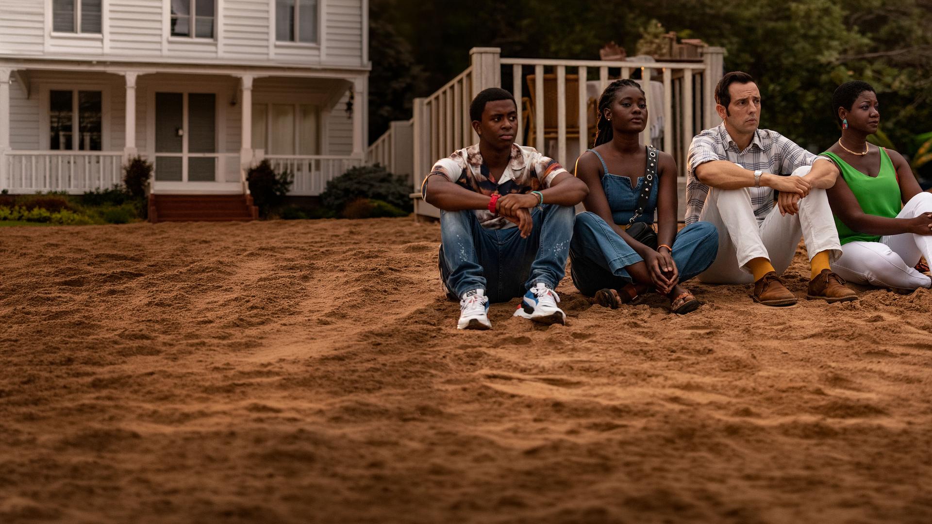 "Death in Paradise - Enttarnt": Officer Marlon Pryce (Tahj Miles), Naomi Thomas (Shantol Jackson) und Darlene Curtis (Ginny Holder) sitzen zusammen mit Detective Neville Parker (Ralf Little) am Strand und blicken in die Ferne.