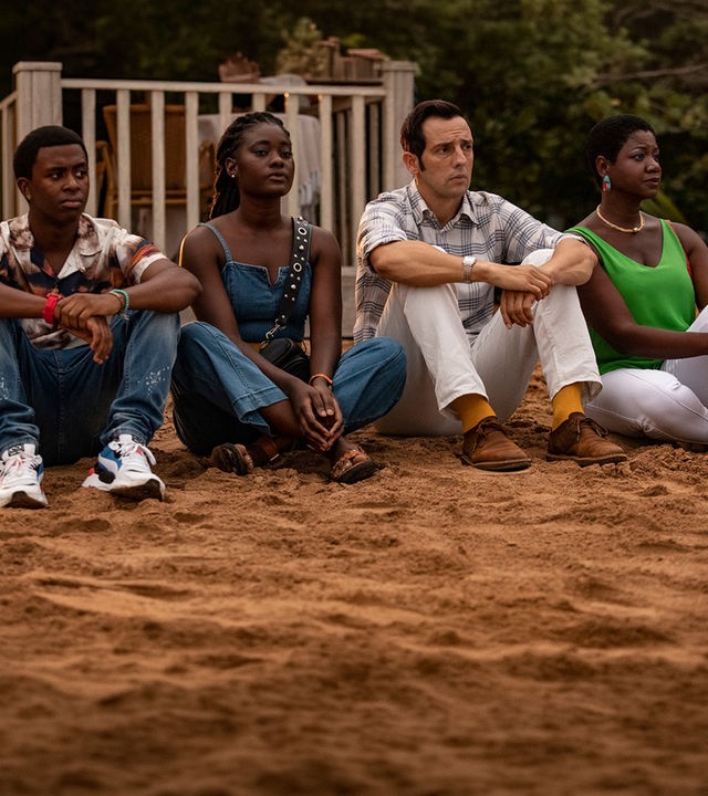 "Death in Paradise - Enttarnt": Officer Marlon Pryce (Tahj Miles), Naomi Thomas (Shantol Jackson) und Darlene Curtis (Ginny Holder) sitzen zusammen mit Detective Neville Parker (Ralf Little) am Strand und blicken in die Ferne.