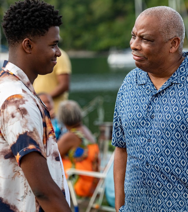 "Death in Paradise - Licht im Dunkeln": Marlon (Tahj Miles) und Commissioner Patterson (Don Warrington) stehen sich auf einem Pier gegenüber. Beide tragen bunte Freizeithemden und schauen sich aufrichtig an.