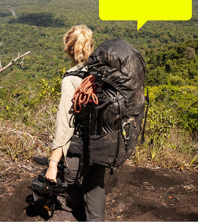 Lucy Shepherd steht auf einer Anhöhe und blickt in ein weites, grünes Tal. Sie trägt einen schwarzen Rucksack auf dem Rücken.
