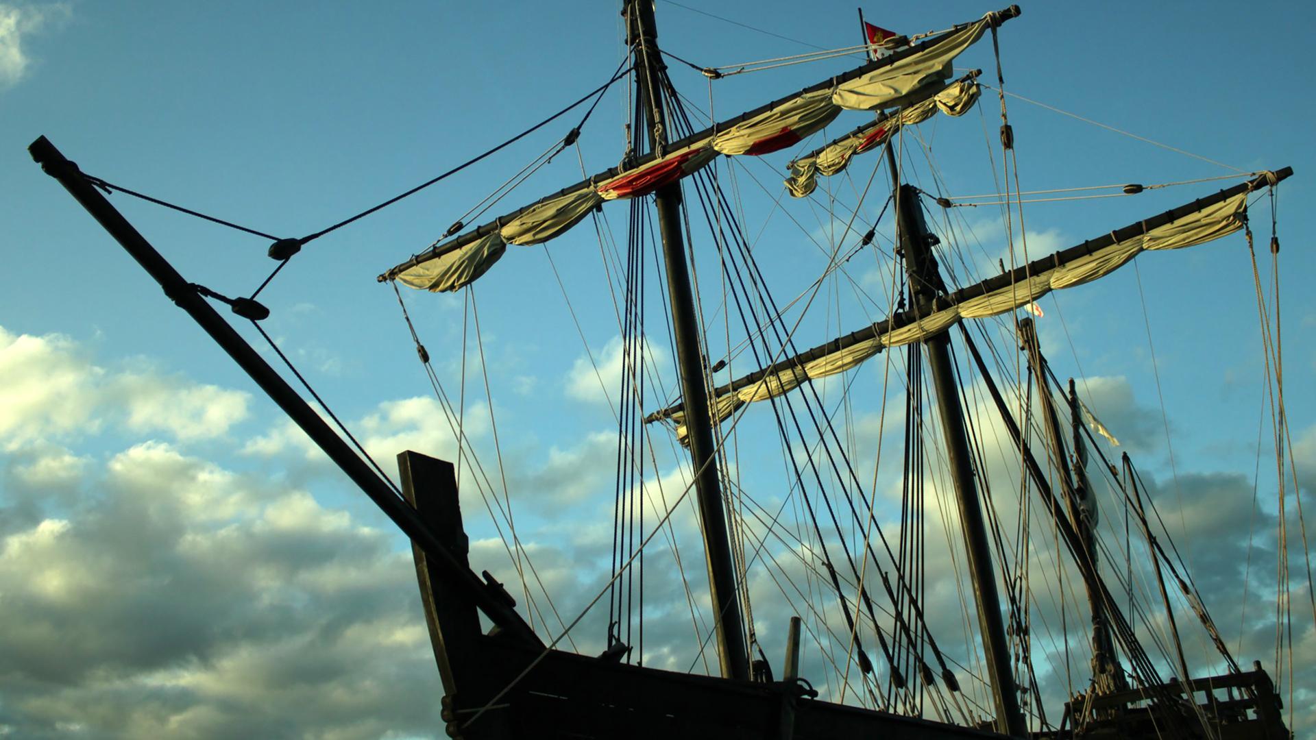 Ein Schiff mit gerefften Segeln vor abendblauem Himmel.