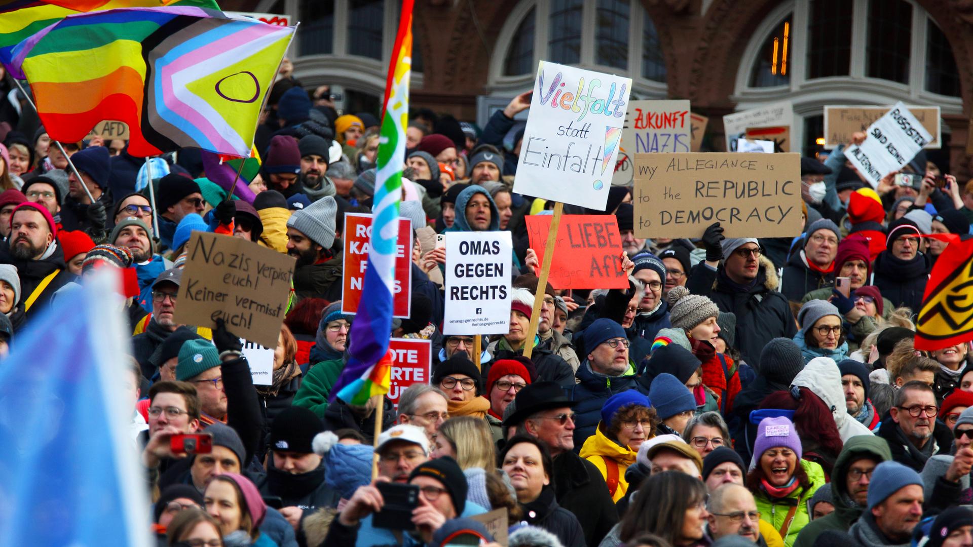 Eine Menschenmenge mit Plakaten und Regenbogenfahnen bei einer Demo gegen rechts.
