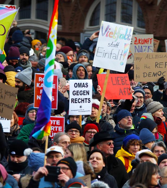 Eine Menschenmenge mit Plakaten und Regenbogenfahnen bei einer Demo gegen rechts.