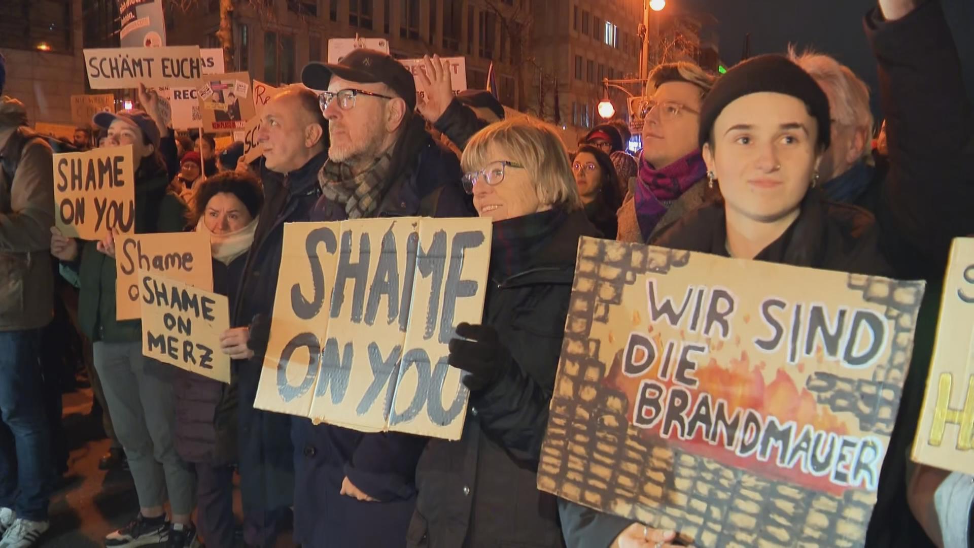 Menschen bei Demo gegen Migrationspolitik in Wiesbaden halten Schilder mit den Aufschriften "Shame on You", "Shame on Merz" und "Wir sind die Brandmauer". 