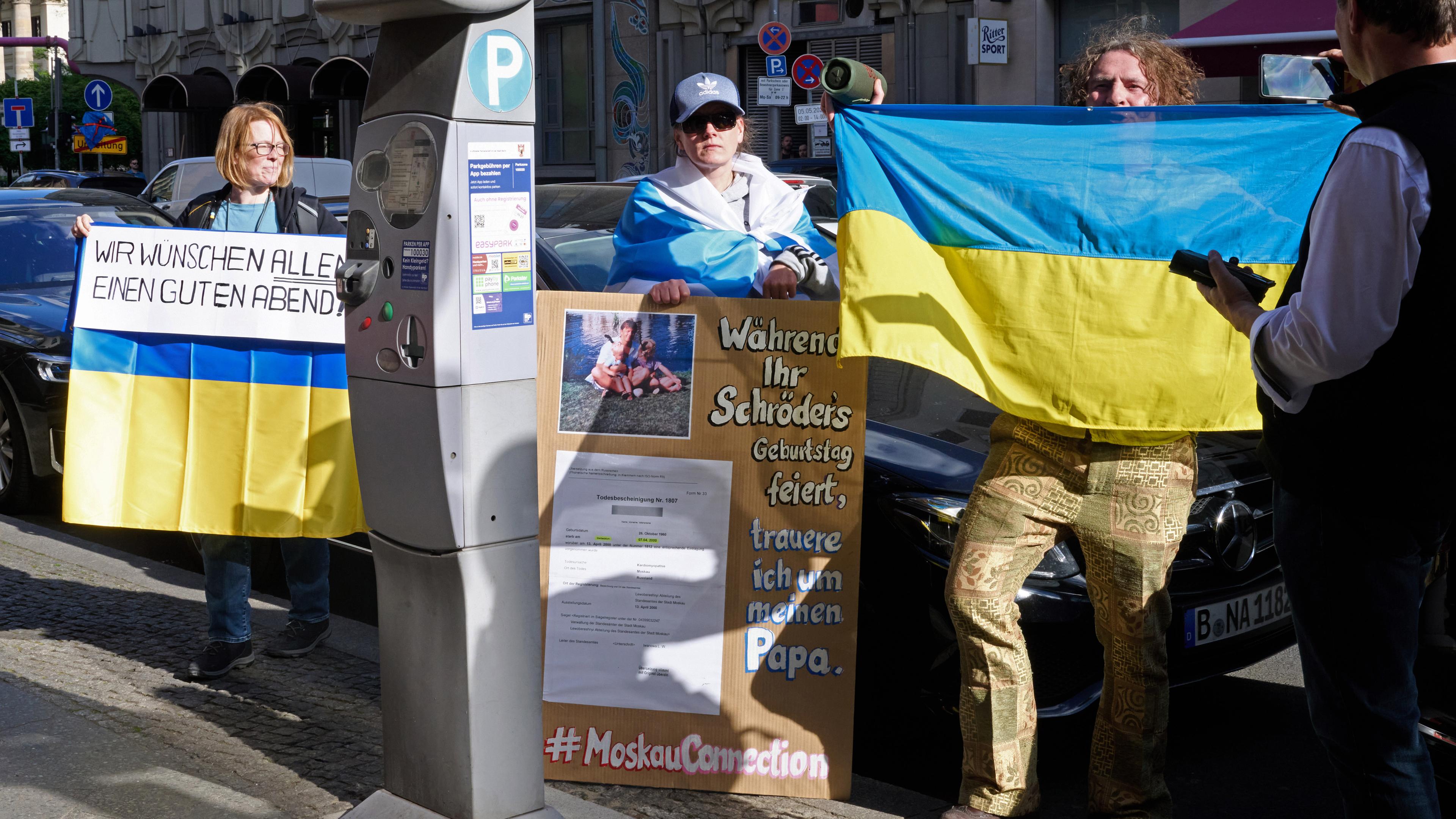 Demonstranten halten ukrainische Fahnen und ein Banner mit der Aufschrift "Wir wünschen allen einen guten Abend" vor dem Restaurant Borchardts, während Altkanzler Schröder dort seinen 80. Geburtstag feiert.