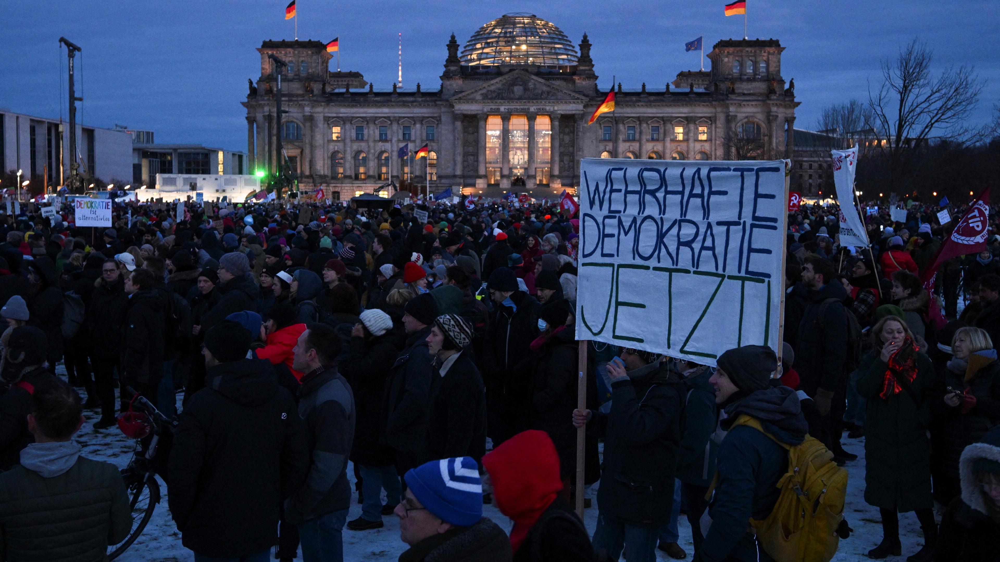 Menschen halten ein Plakat mit der Aufschrift "Wehrhafte Demokratie jetzt", vor dem Reichstagsgebäude in Berlin am 21.01.2024.