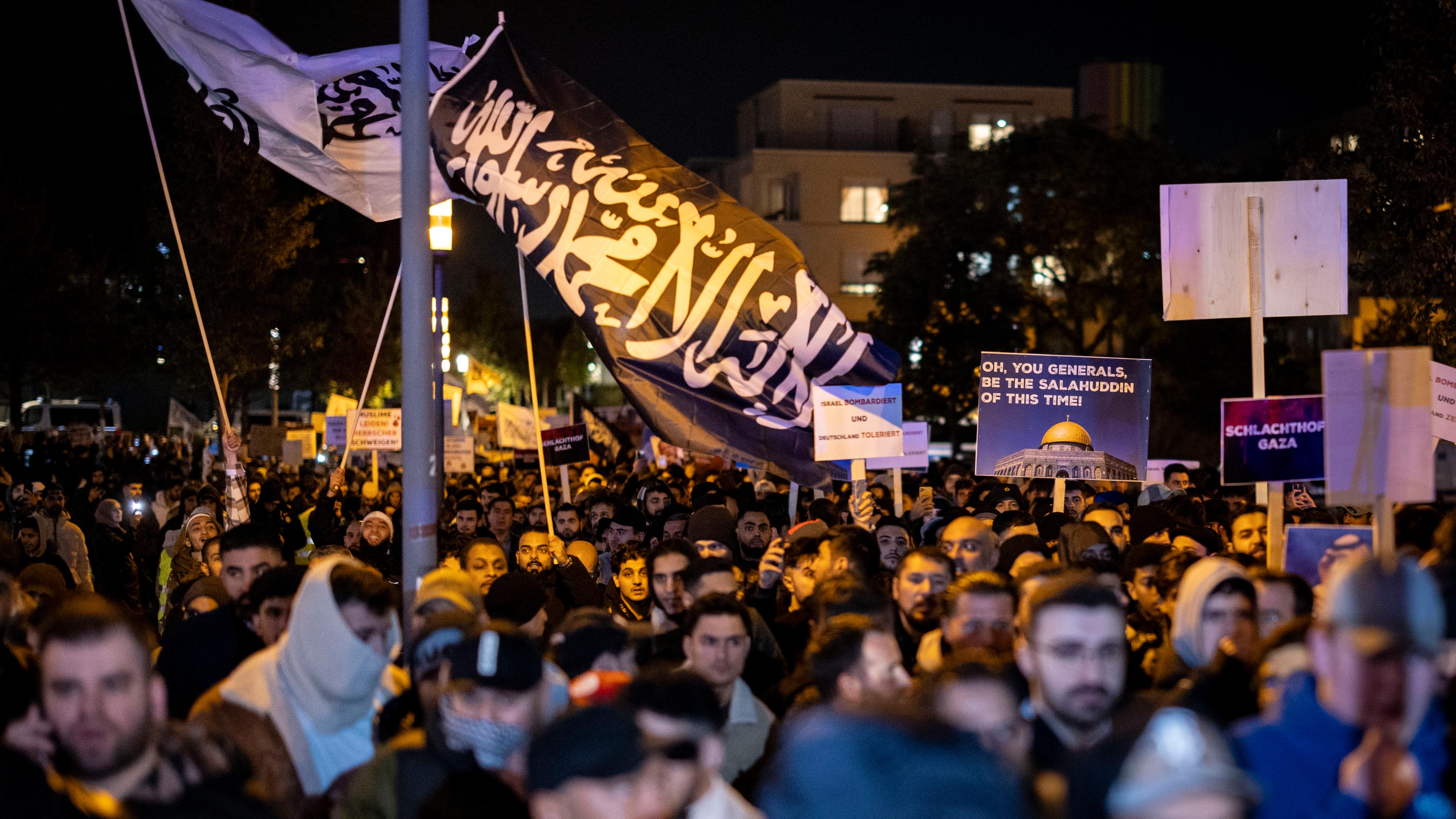 Viele Männer laufen am Abend in Essen bei einer Demonstration. Plakate und Fahnen werden geschwenkt. Es ist die schwarze Flagge von Al-Kaida zu sehen.