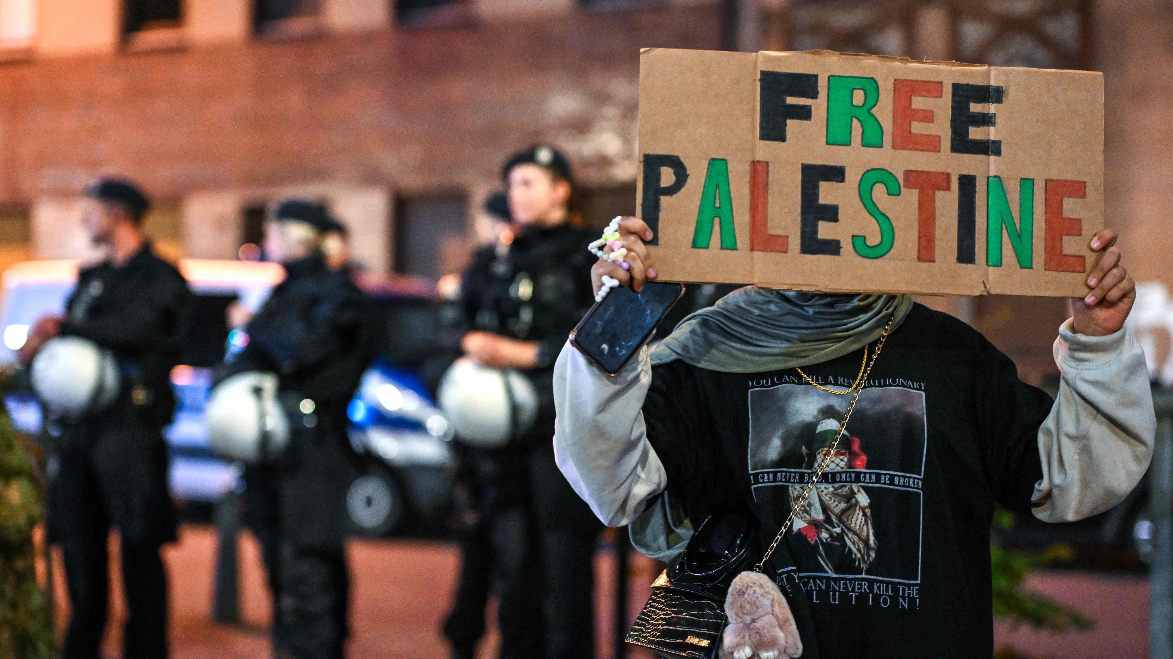 Ein pro-palästinensischer Demonstrant hält während einer "Solidaritätskundgebung mit Gaza" in Duisburg am 9. Oktober 2023 ein Plakat vor Polizeibeamten hoch