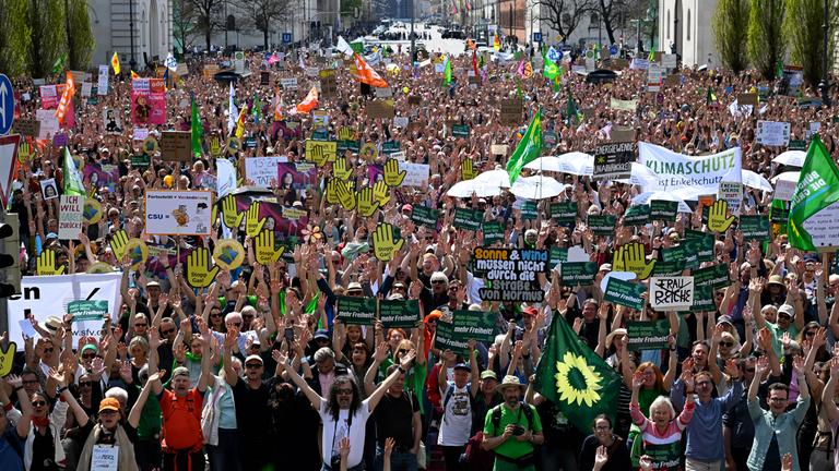 18.04.2026, Bayern, München: Demonstranten heben bei der Demonstration unter dem Motto Erneuerbare Energien verteidigen ihre Hände vor dem Siegestor.