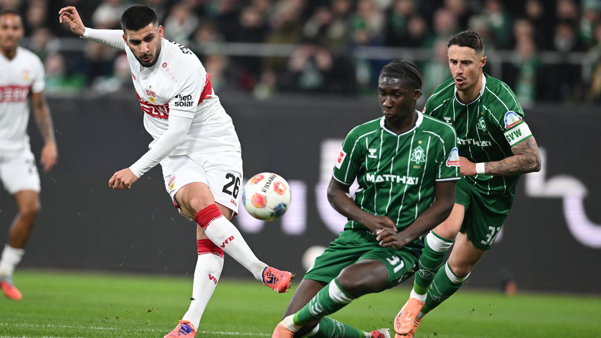 Stuttgarts Stürmer Deniz Undav schießt den Ball in Richtung des Bremer Tors, wird dabei jedoch von Bremens Karim Coulibaly und Marco Friedl bedrängt.