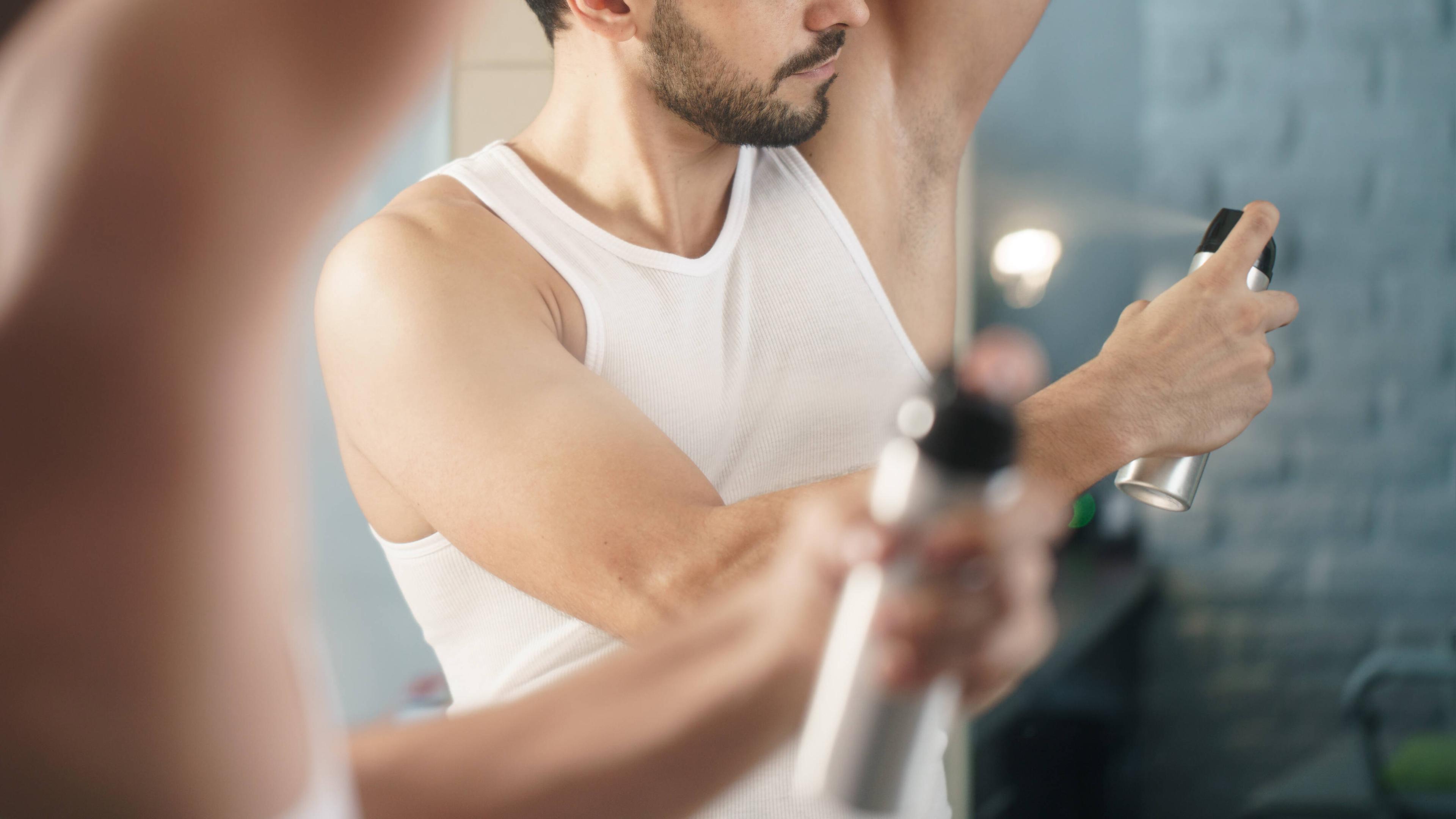 Ein Mann benutzt bei der Körperpflege eine Flasche Deo-Spray