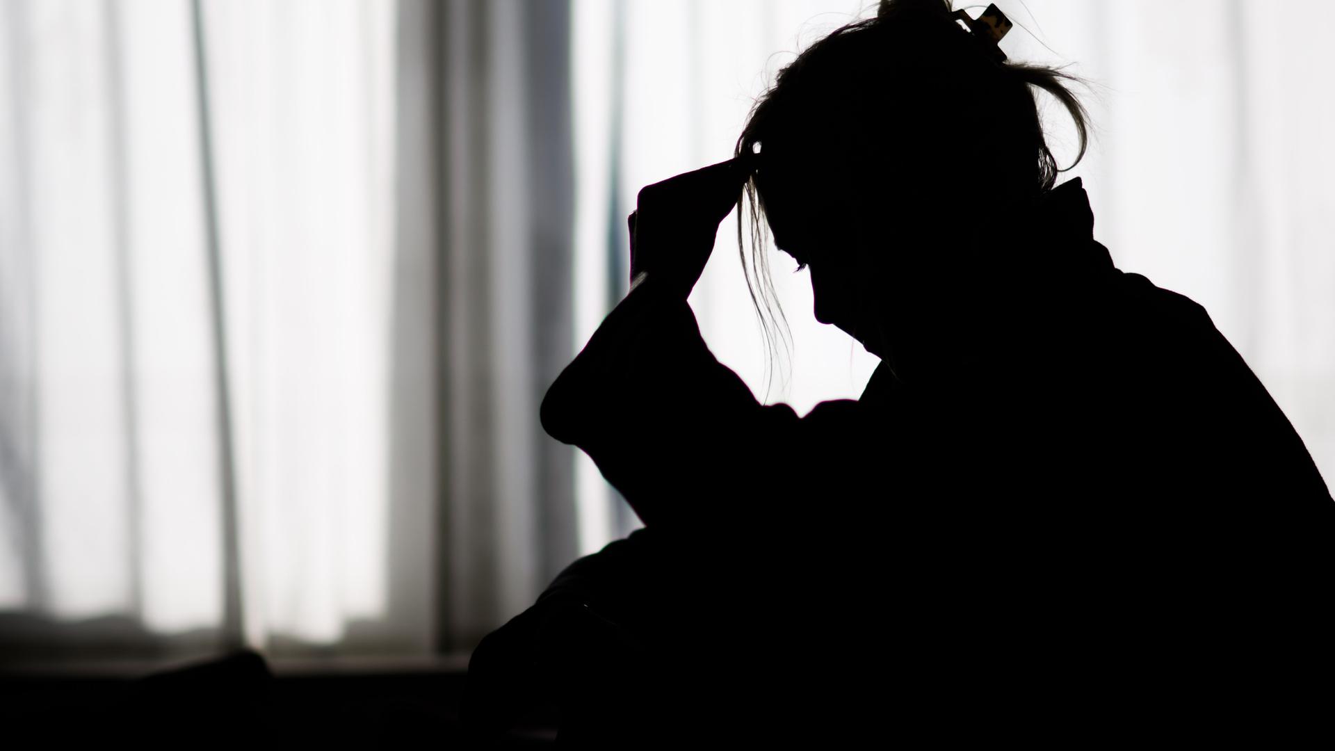 Niedersachsen, Hannover: Die Silhouette einer Frau zeichnet sich vor einer hellen Fensterfront ab (gestellte Szene).