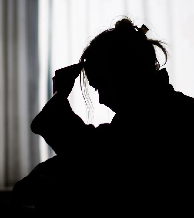 Niedersachsen, Hannover: Die Silhouette einer Frau zeichnet sich vor einer hellen Fensterfront ab (gestellte Szene).