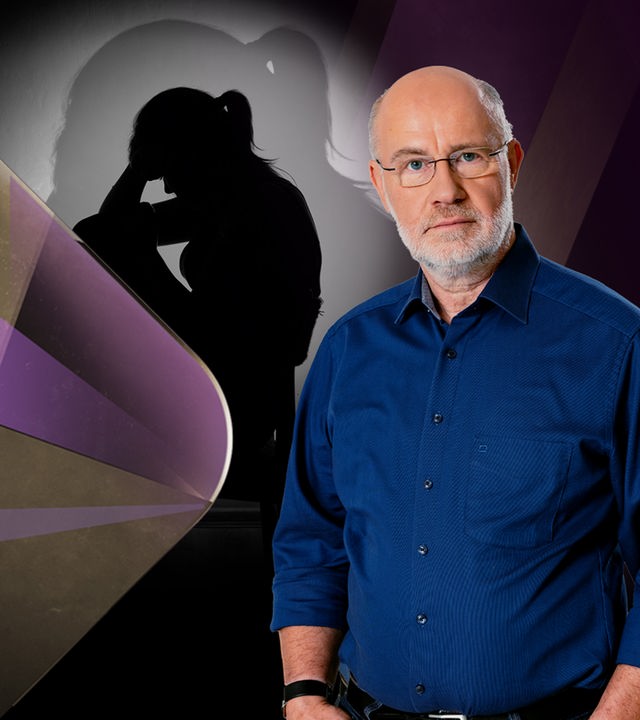 Harald Lesch steht neben trauriger Frau auf Stuhl