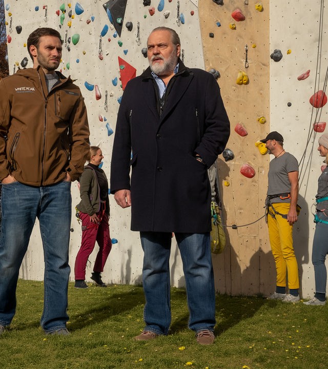 "SOKO Leipzig - Freier Fall": Eric Du Bois (Jonathan Müller) steht mit Hauptkommissar Richard Voss (Jan-Gregor Kremp) im Freien vor einer Kletterwand. Im Hintergrund stehen einige Personen, die sich zum Klettern getroffen haben.