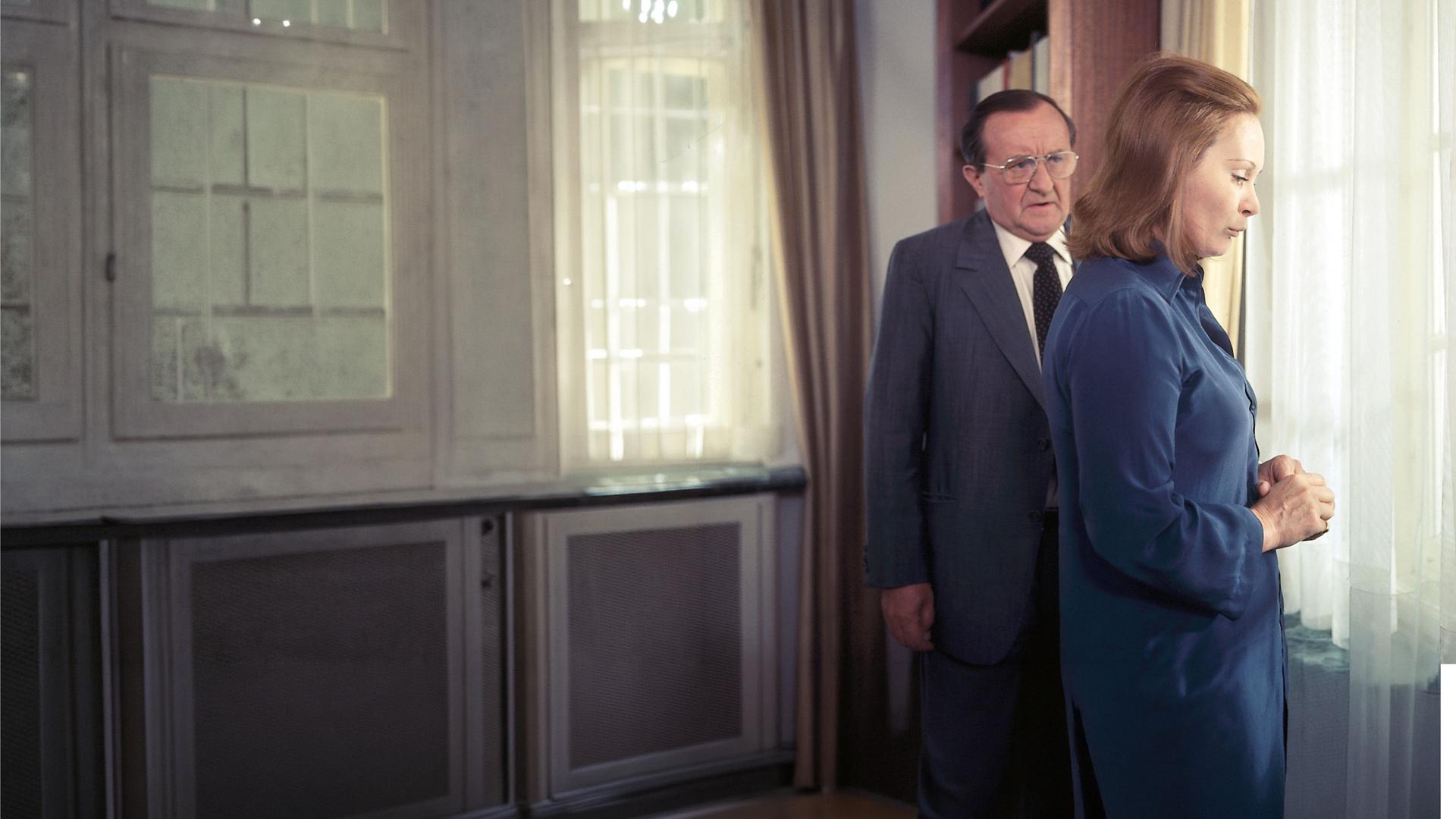 Hauptkomissar Köster (Siegfried Lowitz) und Verena Moldau (Krista Keller) stehen im Wohnzimmer vor einem Fenster. Köster spricht mit ihr und Verena hört zu. Sie schaut nachdenklich nach unten.