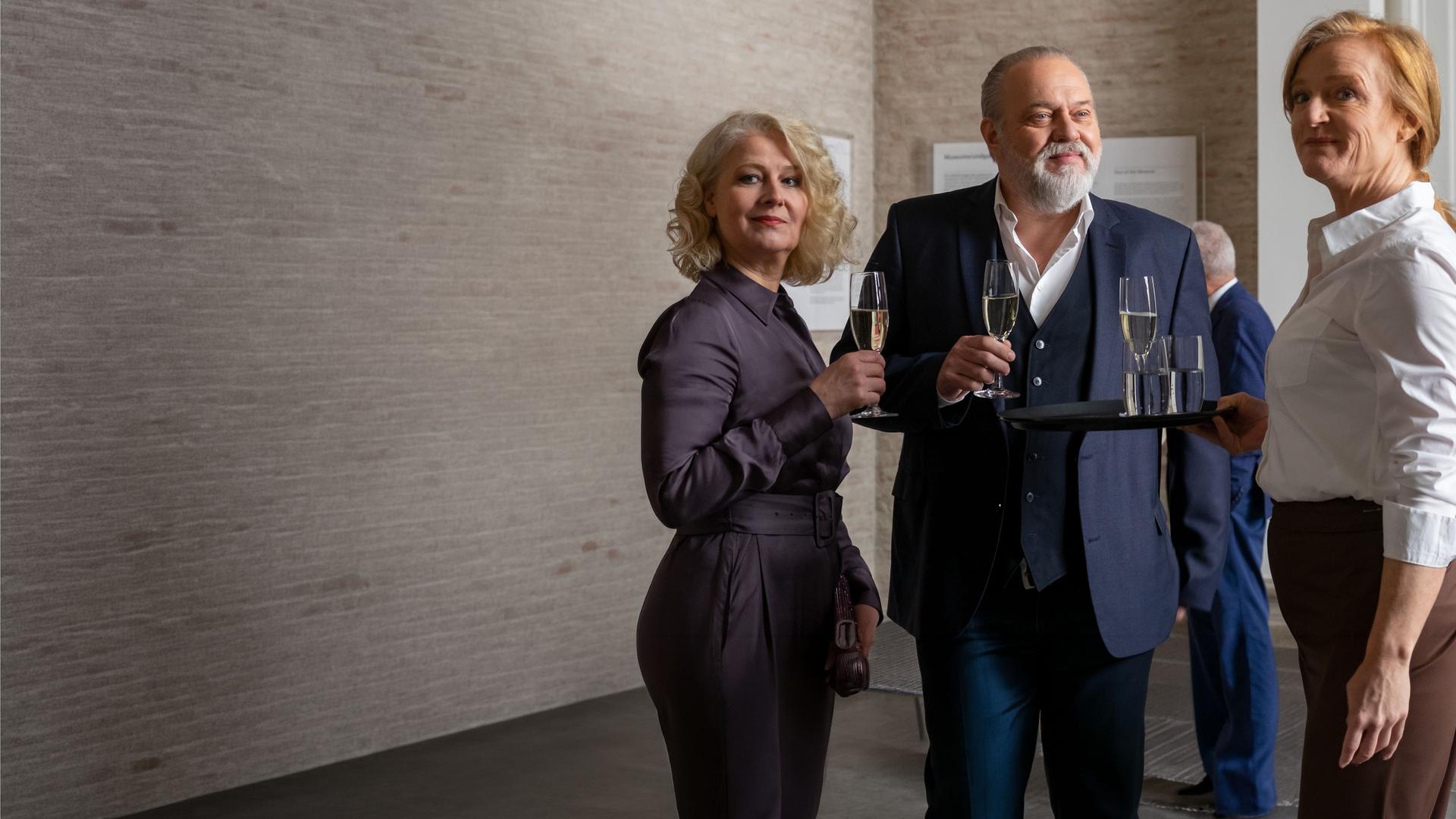 "Der Alte - Verspottung": Dr. Sommerfeld (Christina Rainer), Richard Voss (Jan-Gregor Kremp) stehen bei einem Empfang im Museum mit Sektgläsern in den Händen. Ilse Menzel (Nina Petri) steht neben den beiden und hält ein Tablett mit Getränken in der Hand.