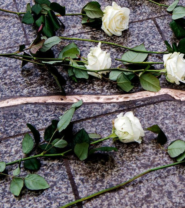 Ein mit Metall ausgegossener Riss im boden des berliner breitscheidplatzes erinnert an die opfer des terroranschlags 2016, darauf liegen weiße Rosen
