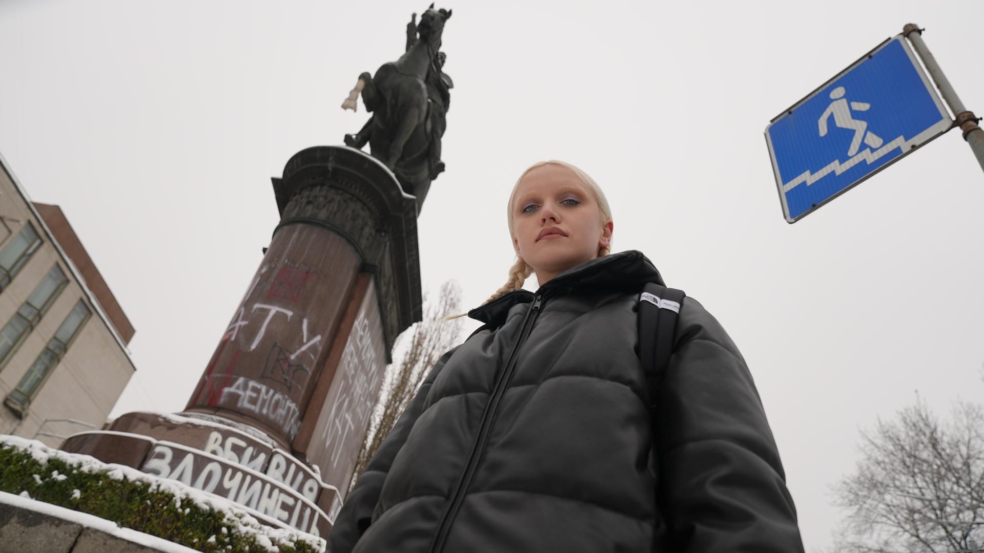 Eine junge Frau vor einer Reiterstatue, die mit Graffiti beschmiert ist.