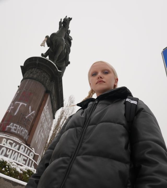 Eine junge Frau vor einer Reiterstatue, die mit Graffiti beschmiert ist.
