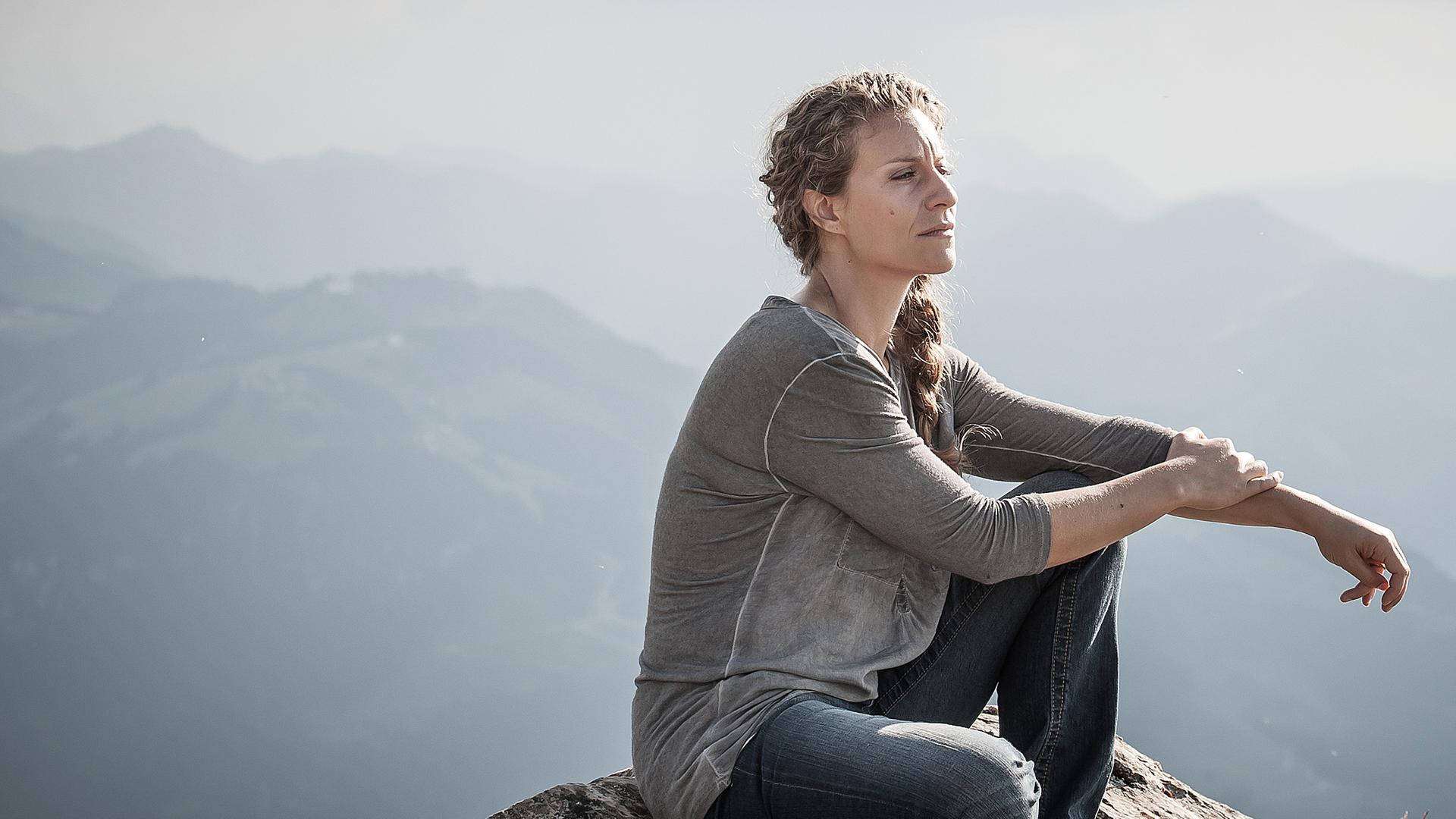 Katharina Selig (Alessija Lause) sitzt auf dem Felsen einer Bergkuppe. 