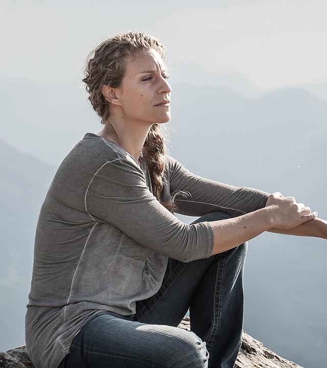 Katharina Selig (Alessija Lause) sitzt auf dem Felsen einer Bergkuppe. 