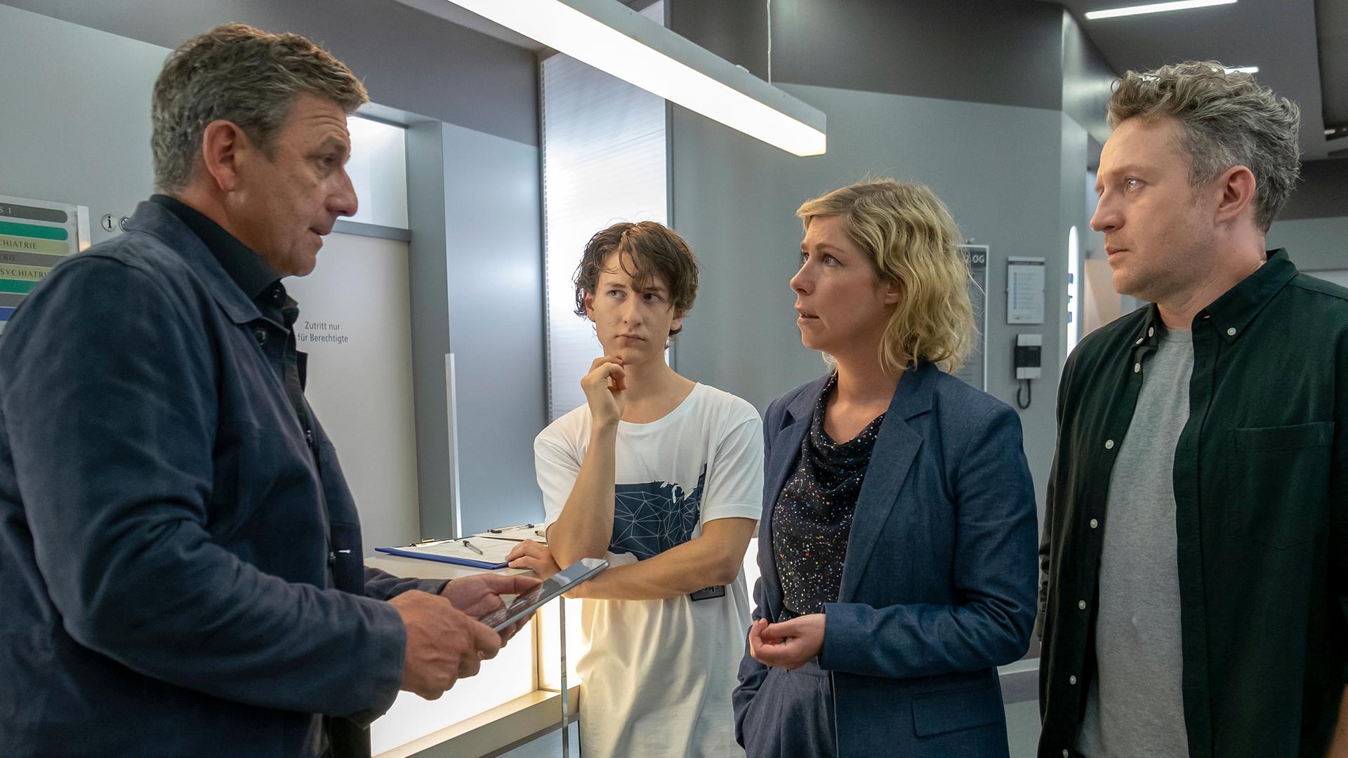 Im Krankenhausflur steht Martin (Hans Gruber) Franz (Josef Heynert), Lisa (Brigitte Zeh) und Lennard (Juri Sam Winkler) gegenüber. Die Familie blickt ihn entsetzt an.