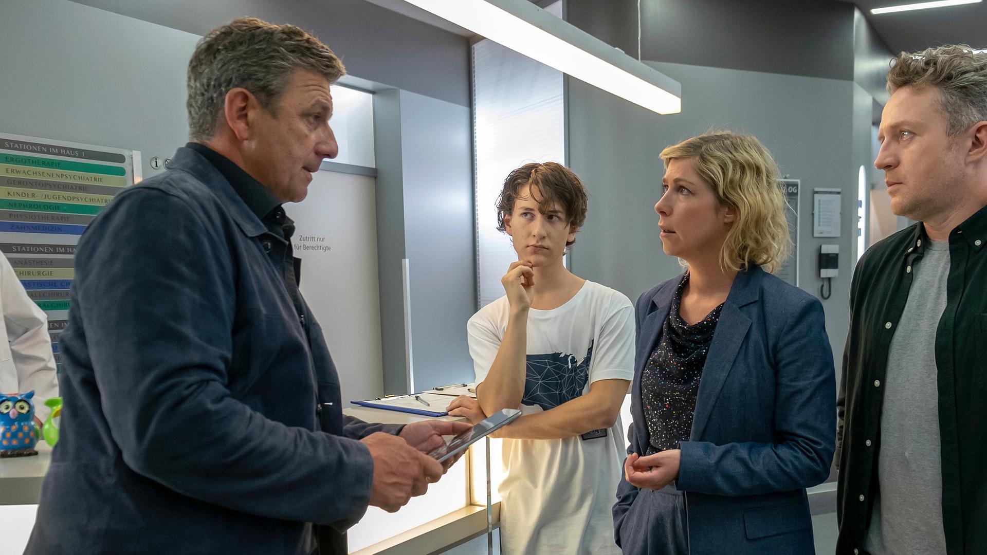 Im Krankenhausflur steht Martin (Hans Gruber) Franz (Josef Heynert), Lisa (Brigitte Zeh) und Lennard (Juri Sam Winkler) gegenüber. Die Familie blickt ihn entsetzt an.