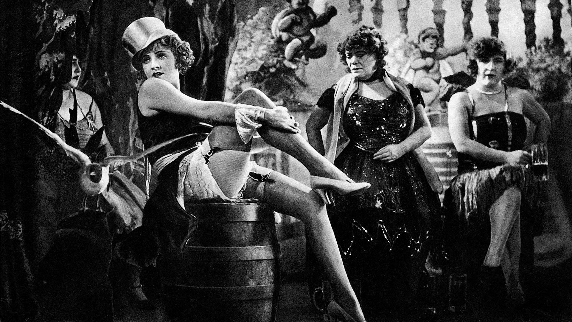 Lola (Marlene Dietrich) räkelt sich auf der Bühne auf einem Faß als Requisit, sie trägt Strapse, ein ärmelloses Oberteil sowie einen Zylinder. Im Bühnenhintergrund treten weitere leichtbekleidete Frauen auf.