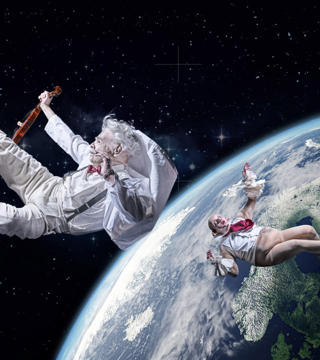 Zwei Personen schweben rücklings im All um die Erde. Ein weiß gekleideter Mann mit Bart hält dabei eine Geige in der Hand. 
