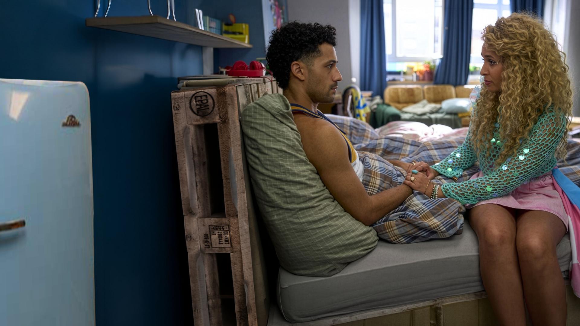 "Ich dich auch! - Der Engel": Yannik (Rojan Juan Barani) sitzt zugedeckt im Bett und schaut ernst zu Sam (Natasha Kimberly), die festlich gekleidet seine Hände hält.