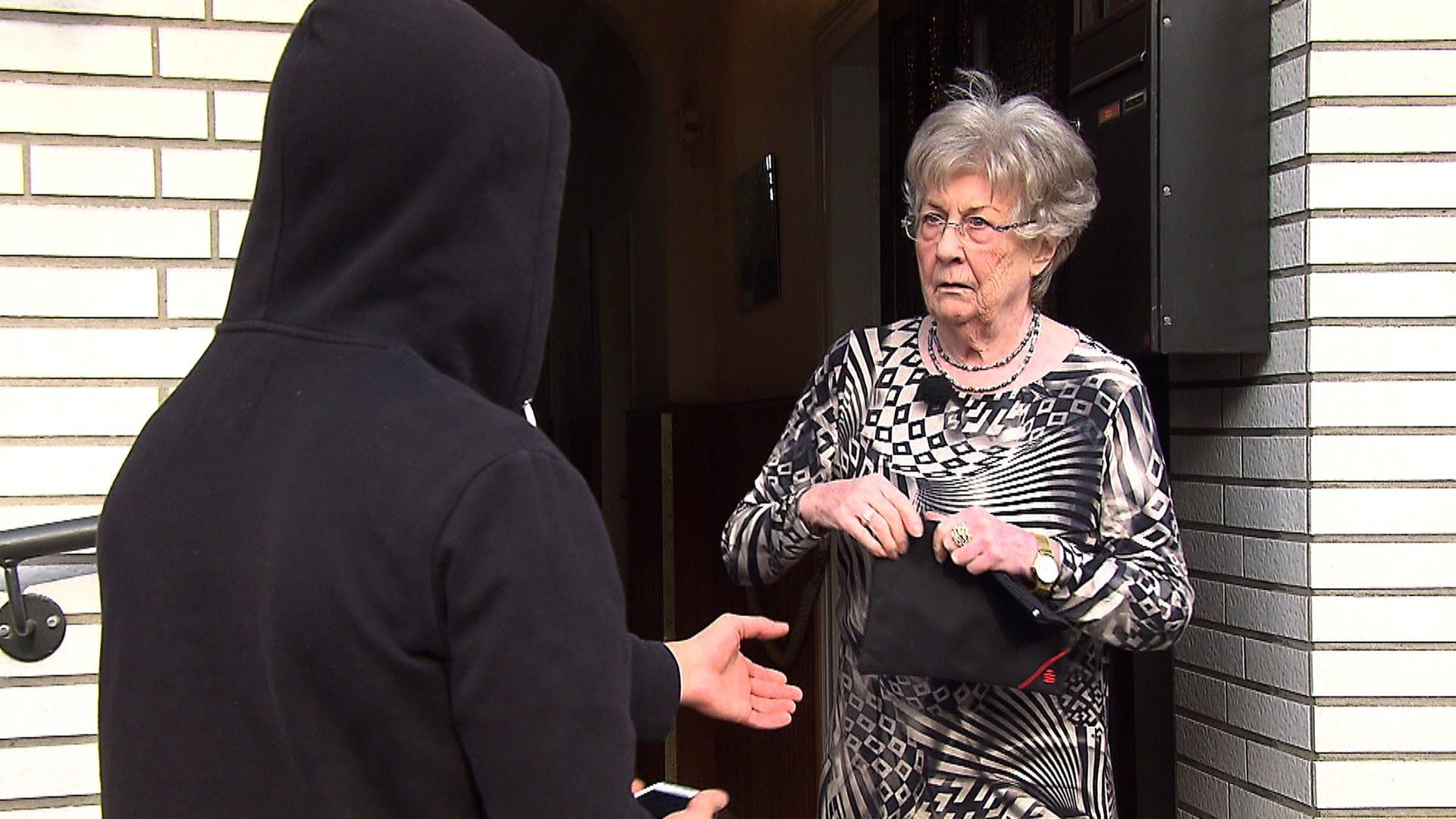 "Der Enkeltrick - Das organisierte Verbrechen am Telefon": Erna Grünsfelder steht vor einer Haustür und schaut eine Person an, die von hinten zu sehen ist und einen schwarzen Kapuzenpullover trägt.
