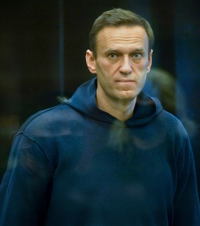 Alexey Nawalny steht im Käfig im Gericht, bekleidet mit einem dunkelblauen Hoody und schaut direkt durch die Glasscheibe in die Kamera.