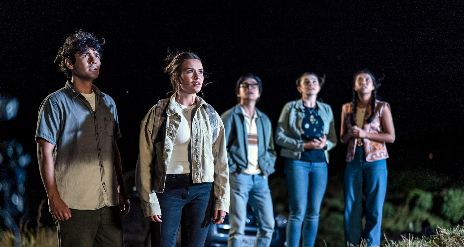 Dan (links), Issie (2.v.l.), Caleb (Mitte), Natasha (2.v.r.) und Caroline (rechts) stehen am Strand und blicken erstaunt in den Abendhimmel.