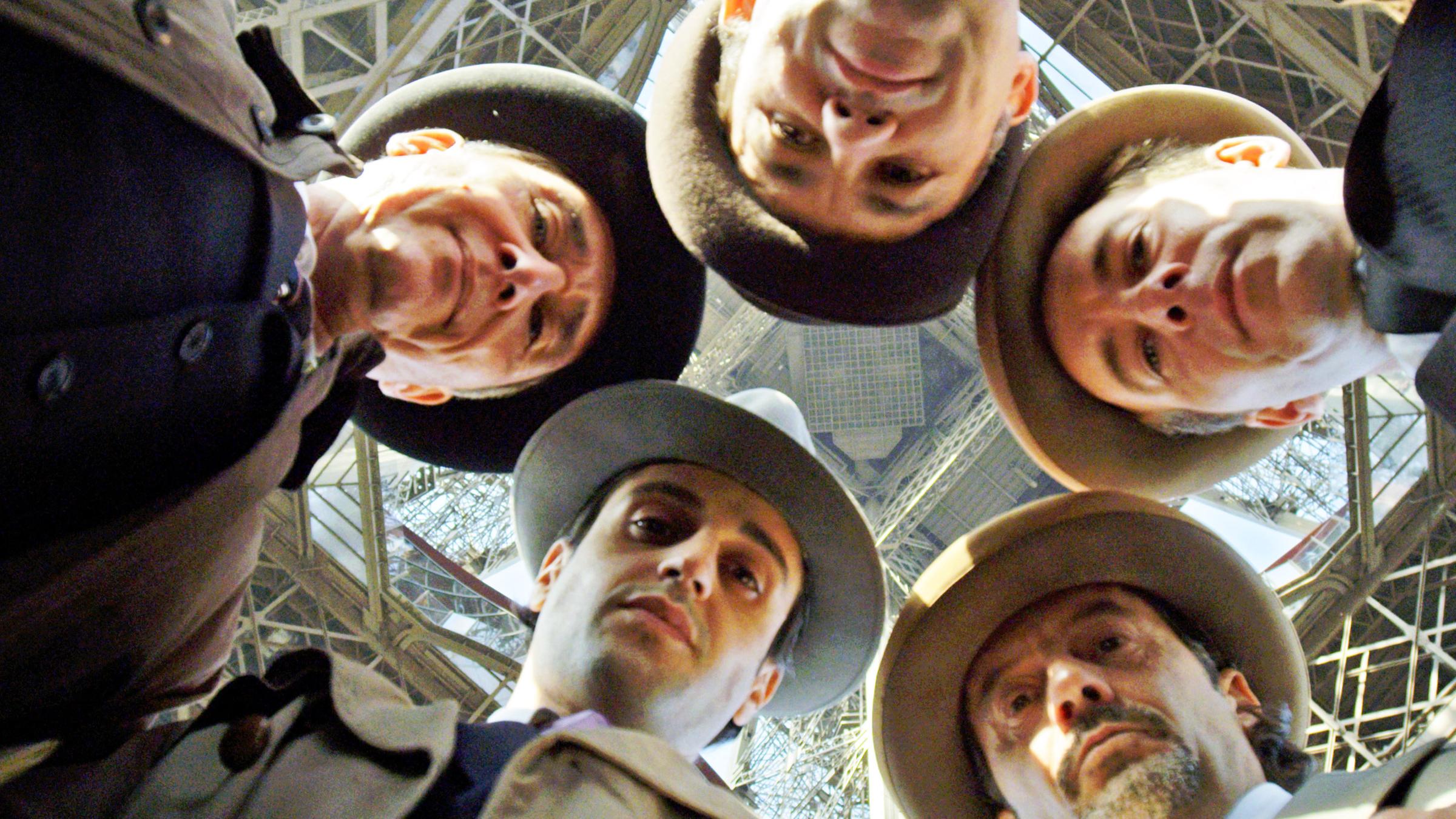 Fünf Männer mit Hut stecken die Köpfe zusammen