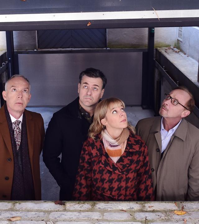 Helmut Zangel (Christoph Süß), Harald Neuhauser (Marcus Mittermeier), Angelika Flierl (Bernadette Heerwagen) und Ludwig Schaller (Alexander Held) blicken aus einem abgesenkten und überdachten Bereich nach oben. Sie sind umgeben von den Wänden einer Villa sowie von einer hohen Hecke.