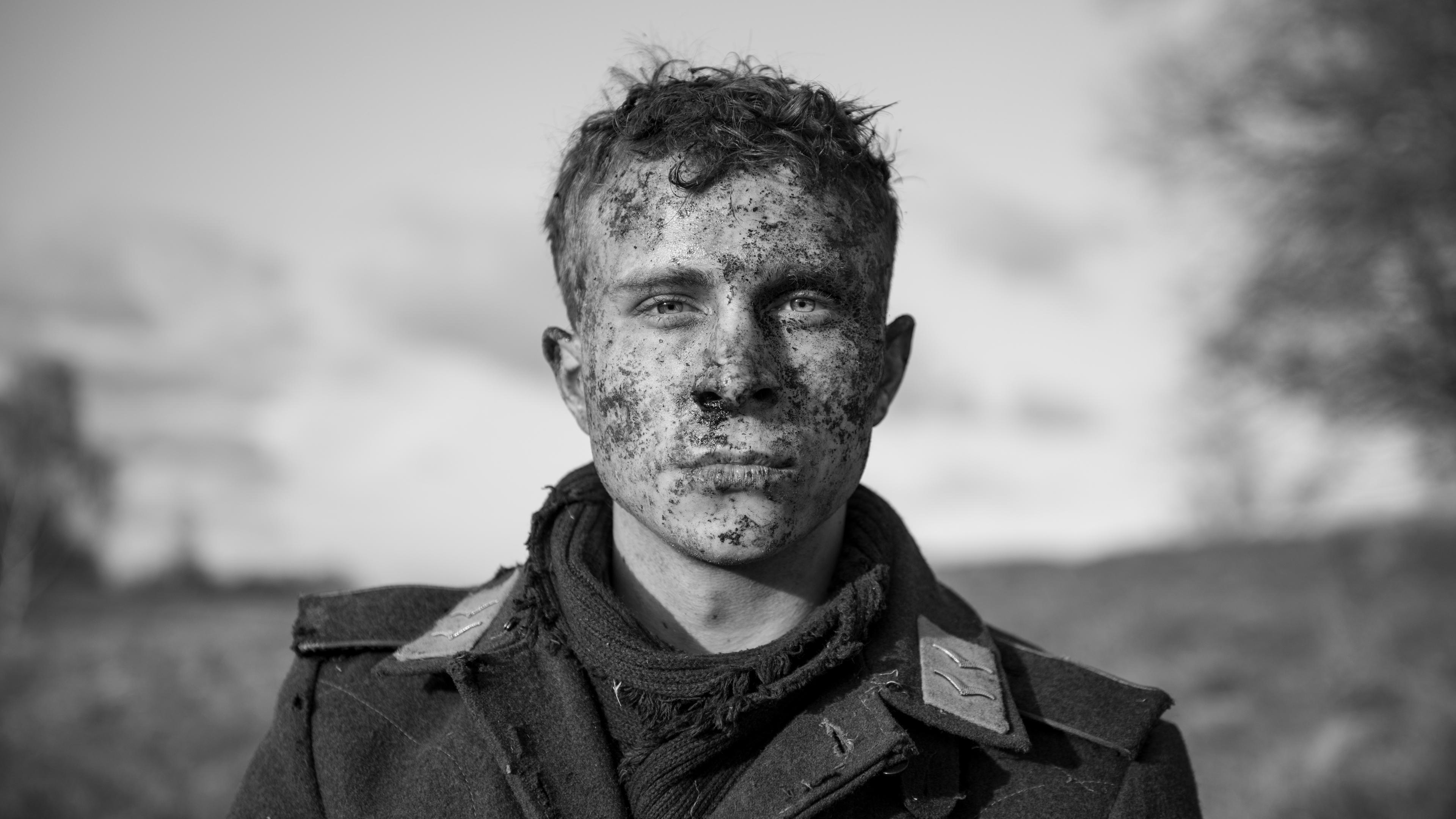 Ein junger Soldat mit dreckverschmiertem Gesicht und mit offenem Uniformkragen blickt ausdruckslos-abwesend in die Kamera nach vorne.