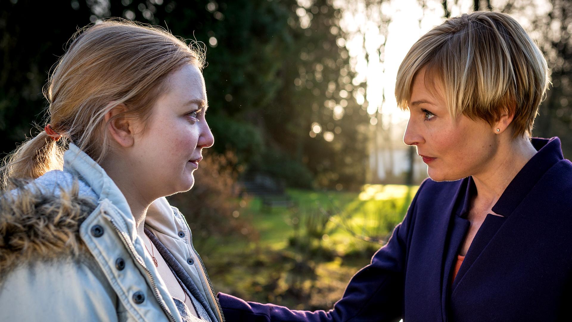 Melanie Hansen (Sanna Englund) steht Jennifer Mikesch (Lilli Fichtner) gegenüber und hat fürsorglich eine Hand auf Jennifers Oberarm gelegt. 