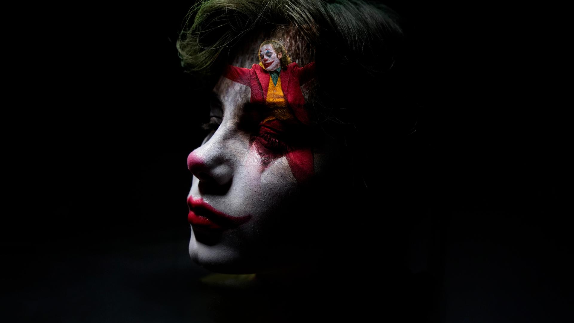 Nahaufnahme eines als Clown geschminkten Jungen. Sein Gesicht ist zur Hälfte im Dunkeln, auf seiner Stirn ist klein eine Szene des tanzenden Jokers eingeblendet.