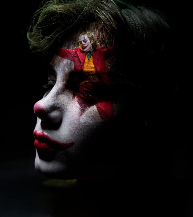 Nahaufnahme eines als Clown geschminkten Jungen. Sein Gesicht ist zur Hälfte im Dunkeln, auf seiner Stirn ist klein eine Szene des tanzenden Jokers eingeblendet.