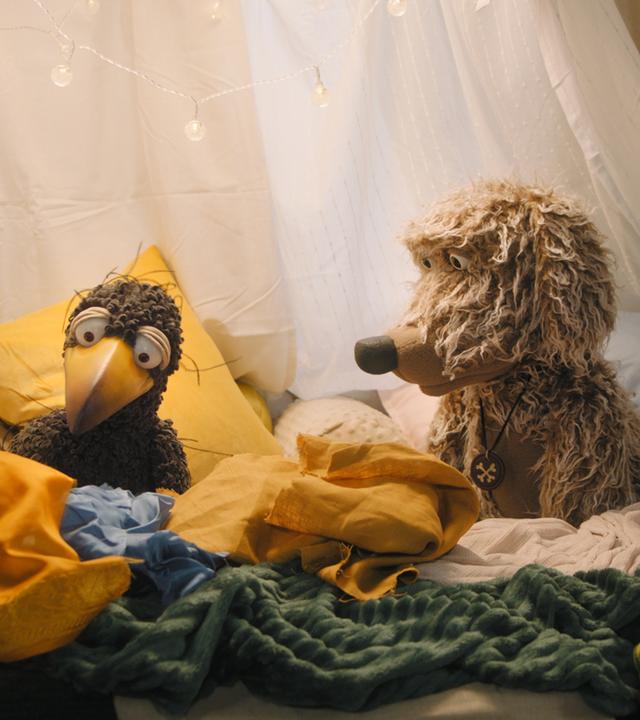 Rabe Rudi sitzt mit Hund Buffo in der gemütlichen Kuschelecke.
