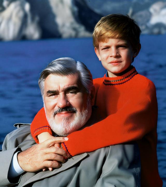 "Der kleine Lord": Carl Schneibel (Mario Adorf) wird liebevoll von Christian (Francesco De Pasquale) umarmt, der hinter ihm steht. Im Hintergrund sind das Meer und Felsen zu sehen.