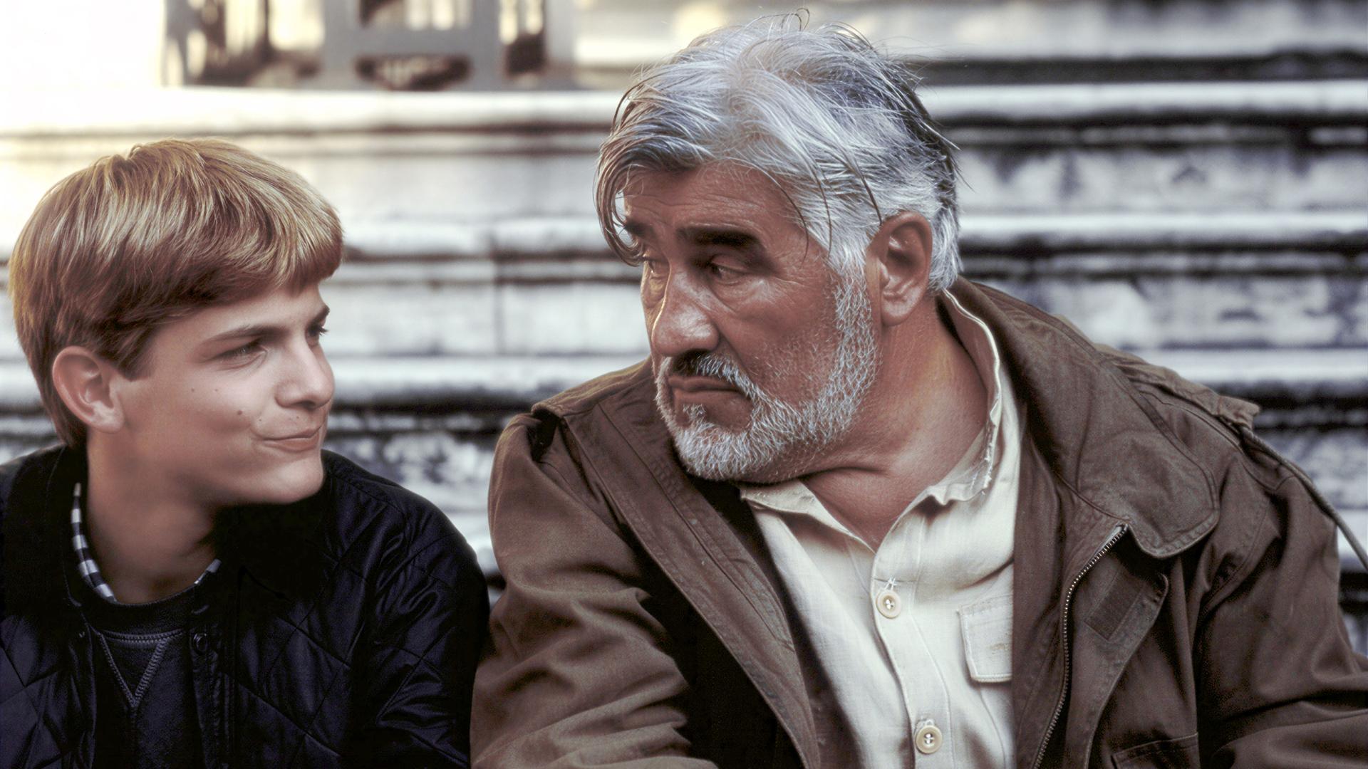 "Der kleine Lord - Retter in der Not": Christian (Francesco De Pasquale) und Carl Schneibel (Mario Adorf) sitzen nebeneinander vor einer Treppe und schauen sich gegenseitig an.