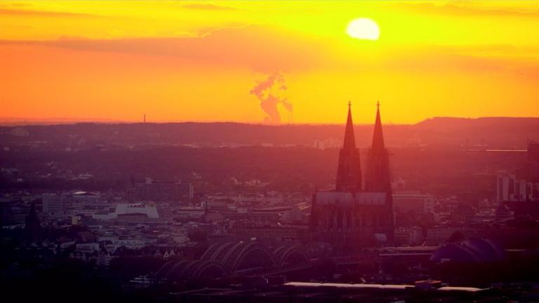 Der Kölner Dom von Osten gesehen im Sonnenuntergang. Davor: Eisenbahnbrücke und Hauptbahnhof.