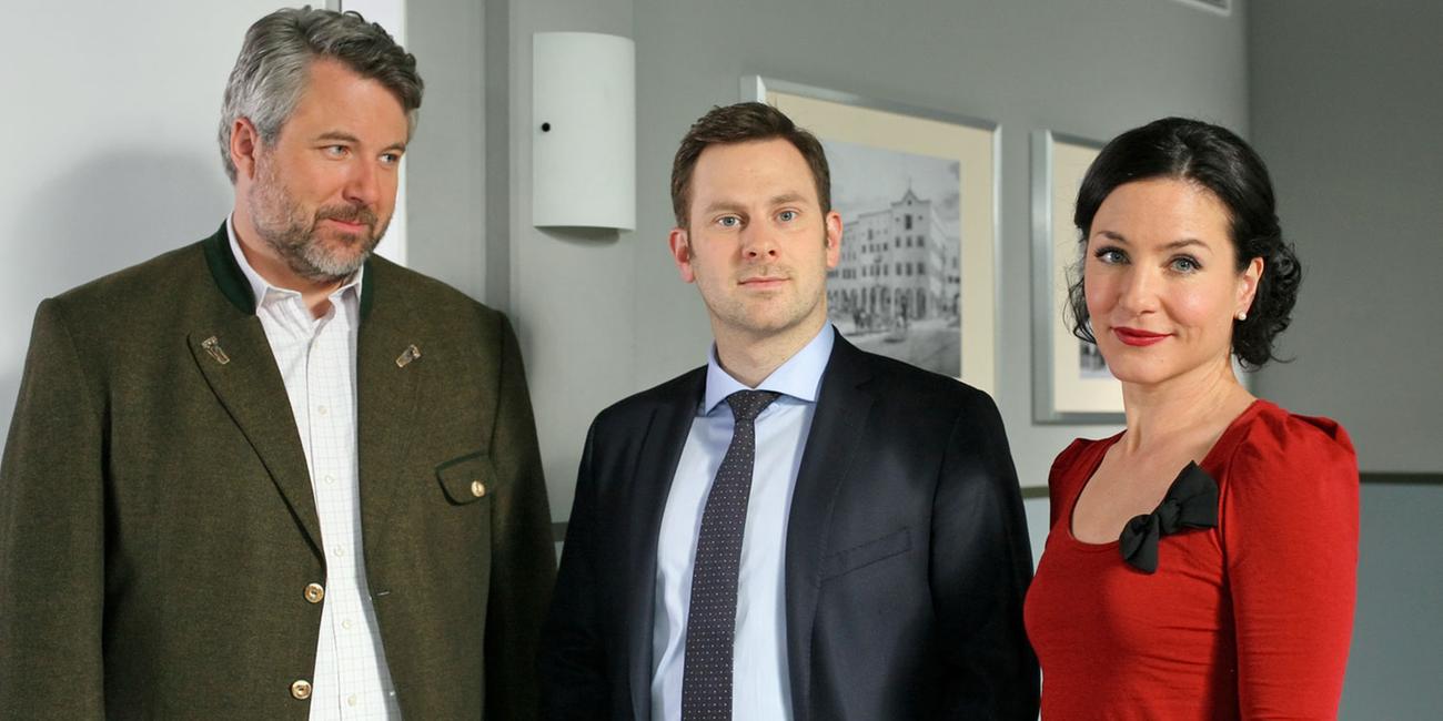 "Die Rosenheim-Cops - Der König kommt": Im Flur des Kommissariats stehen die Kollegen Stadler (Dieter Fischer), Sebastian König (Mark-Alexander Solf) und Sekretärin Stockl (Marisa Burger).