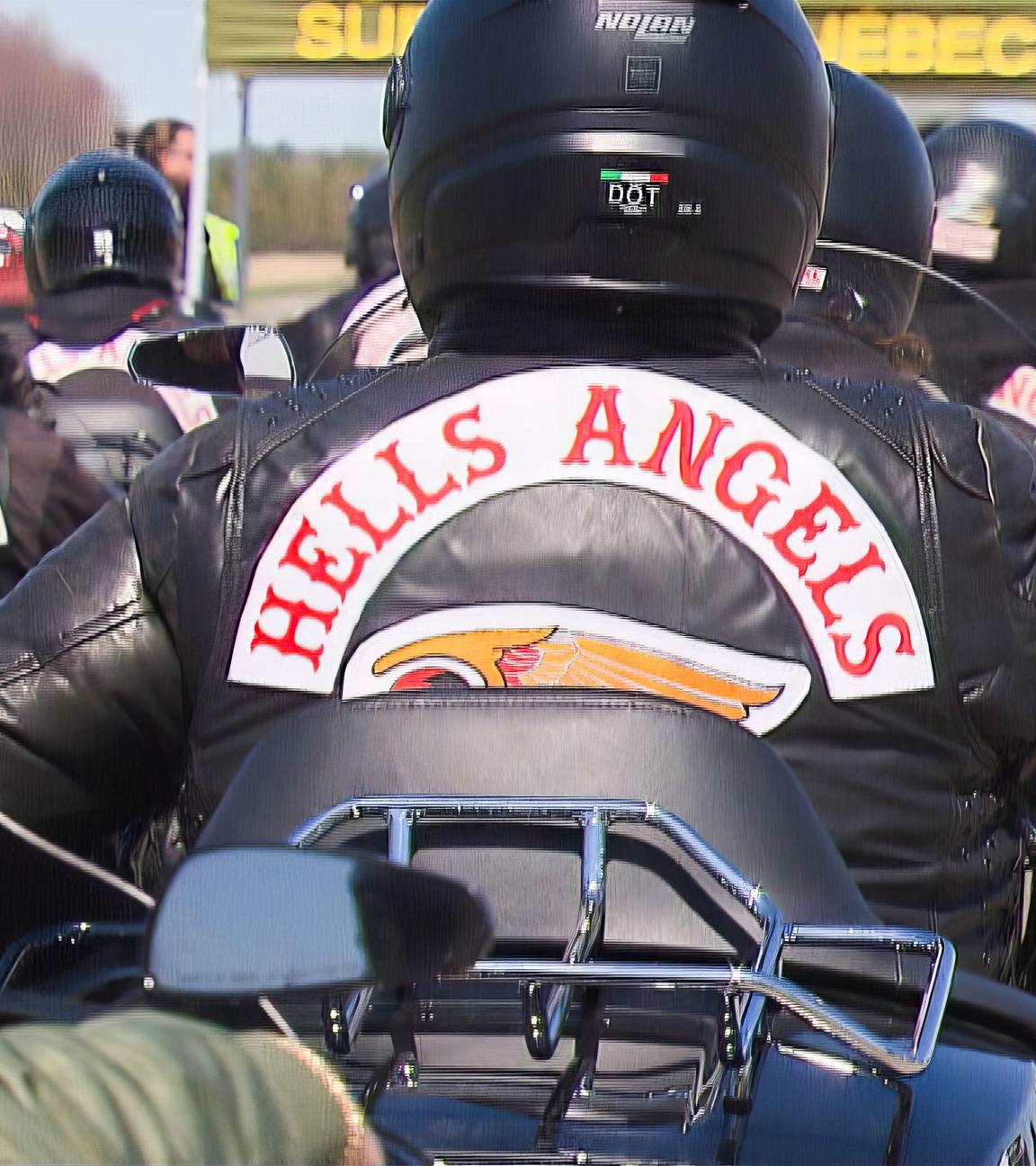 Viele Motorradfahrer mit Lederjacken, auf denen "Hells Angels" steht, fahren auf einer Straße weg von von der Kamera.