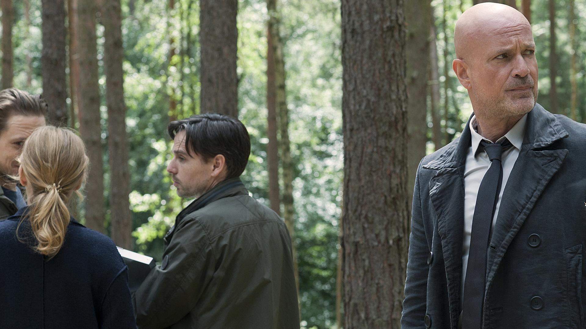 Bruno Schumann (Christian Berkel) steht gemeinsam mit einigen Kollegen im Wald