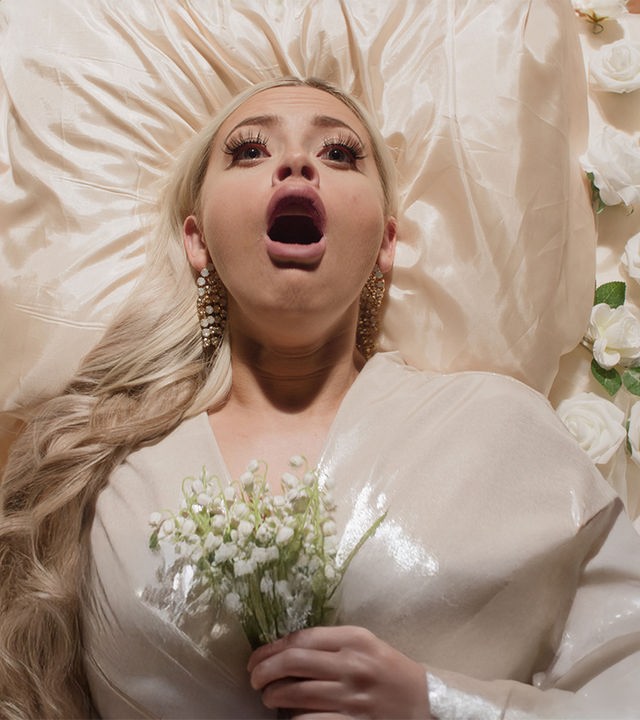 "Requiem for Selina - Der letzte Akt": Blick von oben: Selina (Elli Rhiannon Müller Osborne) liegt auf einem weißen Bett, umringt von weißen Rosen. Sie trägt ein weißes, schimmerndes Kleid. Ihre Augen und ihr Mund sind weit geöffnet.