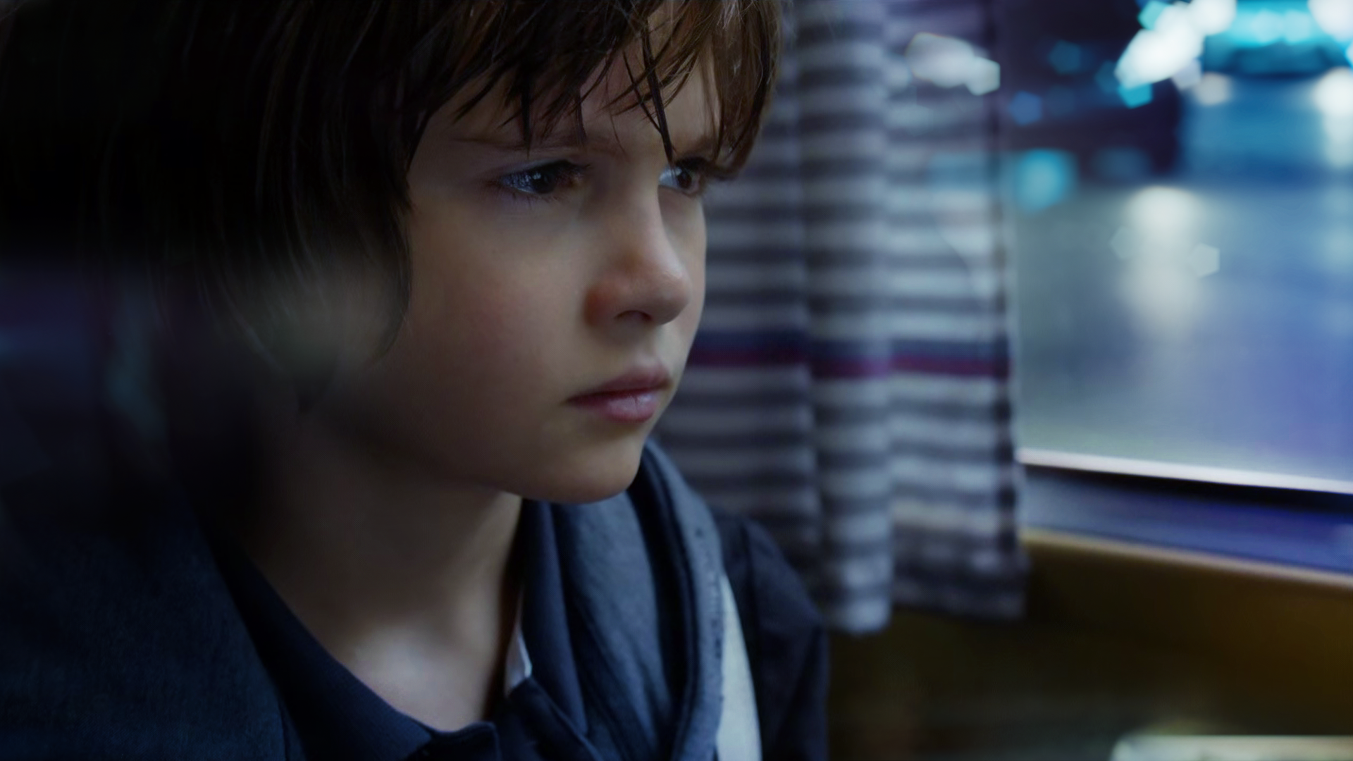 Ein Junge ist als Nahaufnahme vor einem Fenster zu erkennen. Draußen ist es dunkel.