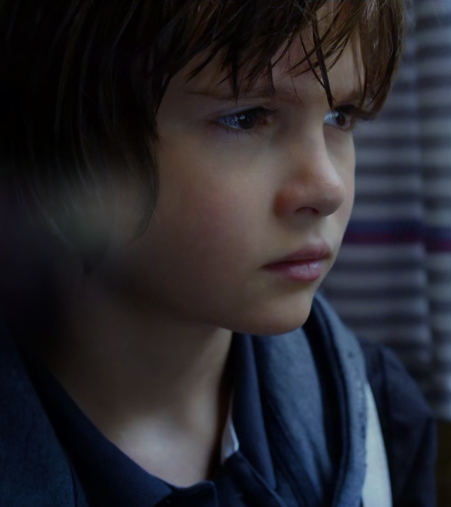 Ein Junge ist als Nahaufnahme vor einem Fenster zu erkennen. Draußen ist es dunkel.